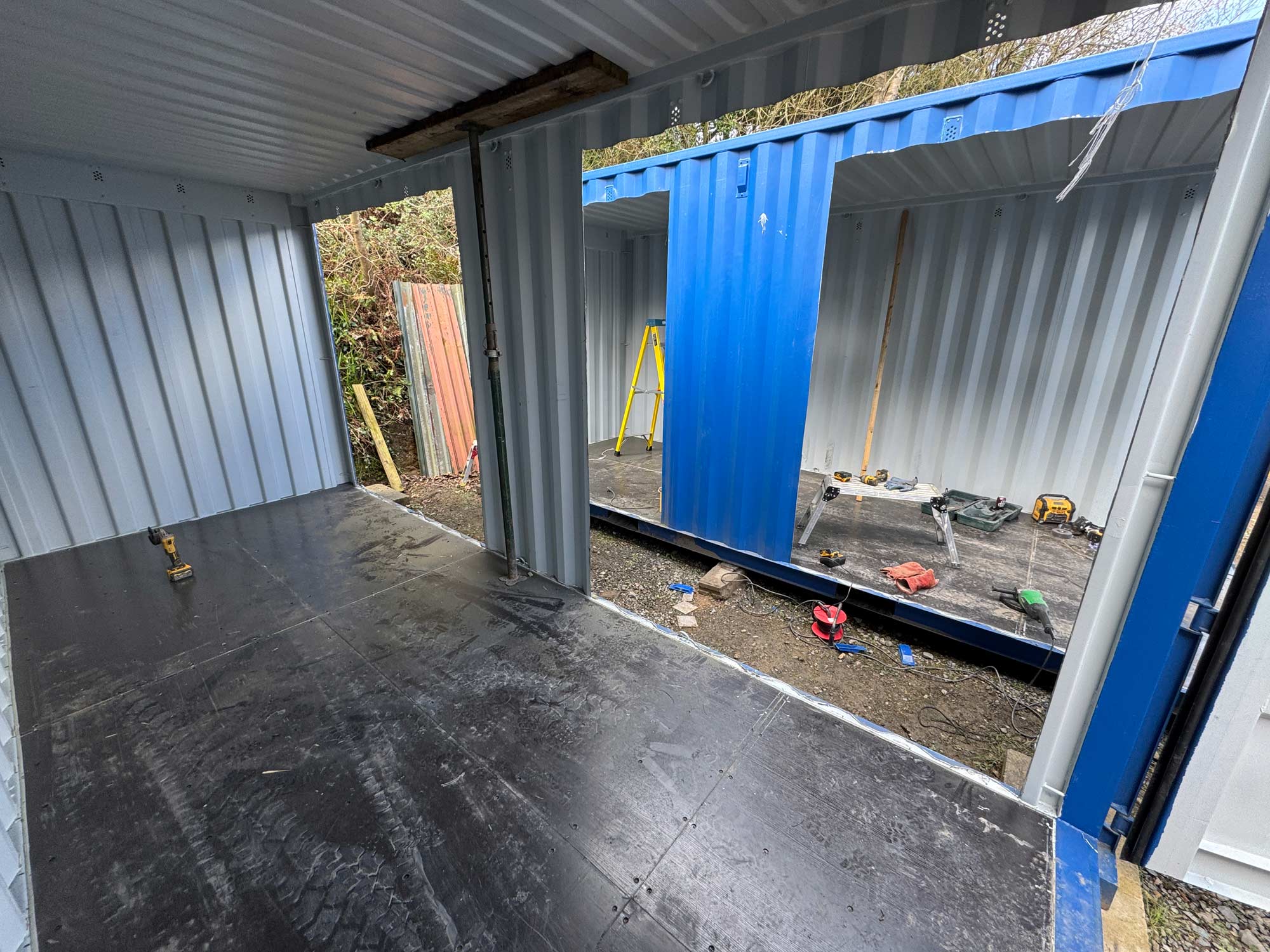 Bespoke shipping container conversion in progress, sparks flying from a cut
